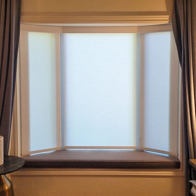White shades on a bay window framed by drapery