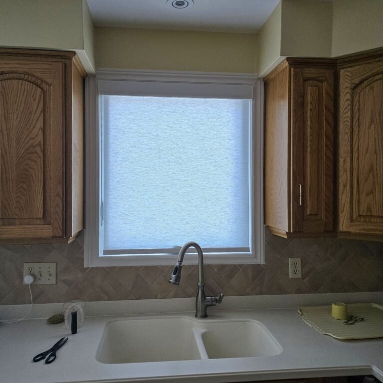 Roller shade on a kitchen window above the sink between wood cabinets