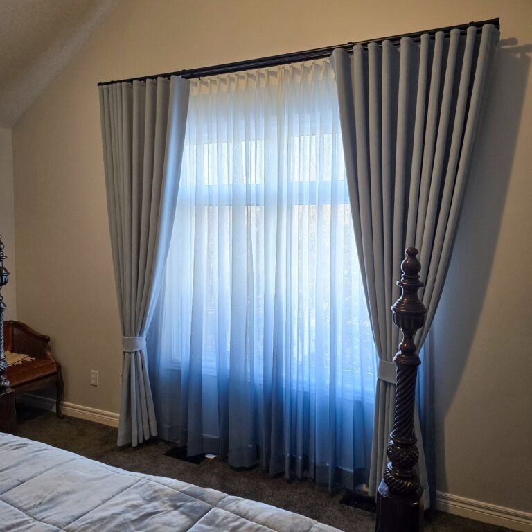 Sheer curtains and grey drapery panels framing a bedroom window