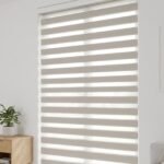 White zebra blinds on a tall living room window with a plant
